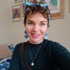 A smiley girl with short curly hair wearing a light blue bandana with matching sea shell earrings.