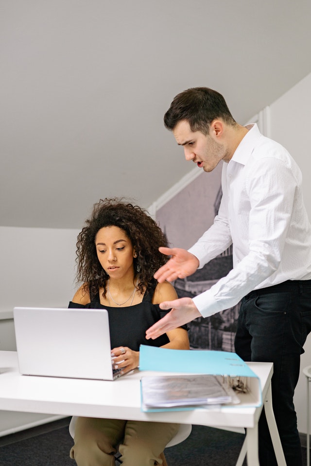 man yelling at woman seated at desk