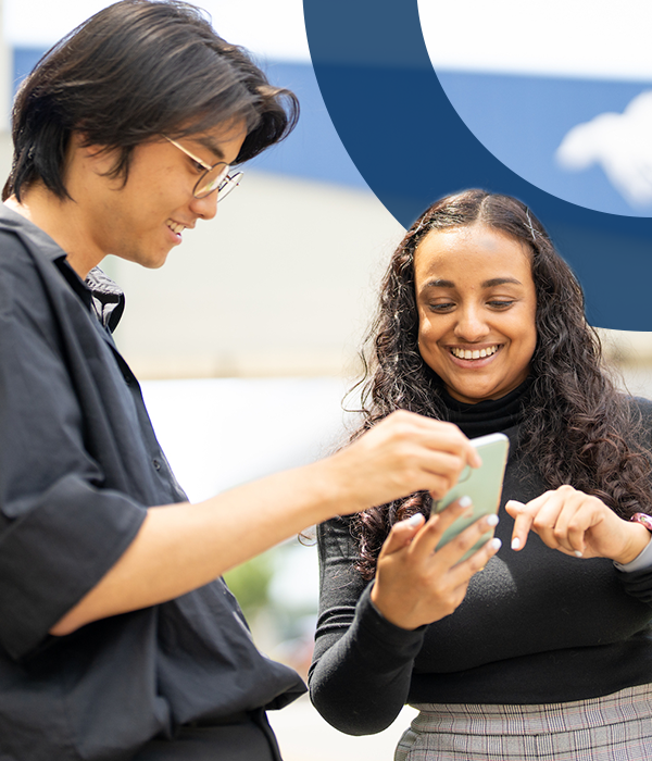 Two students looking at a smartphone together on campus.